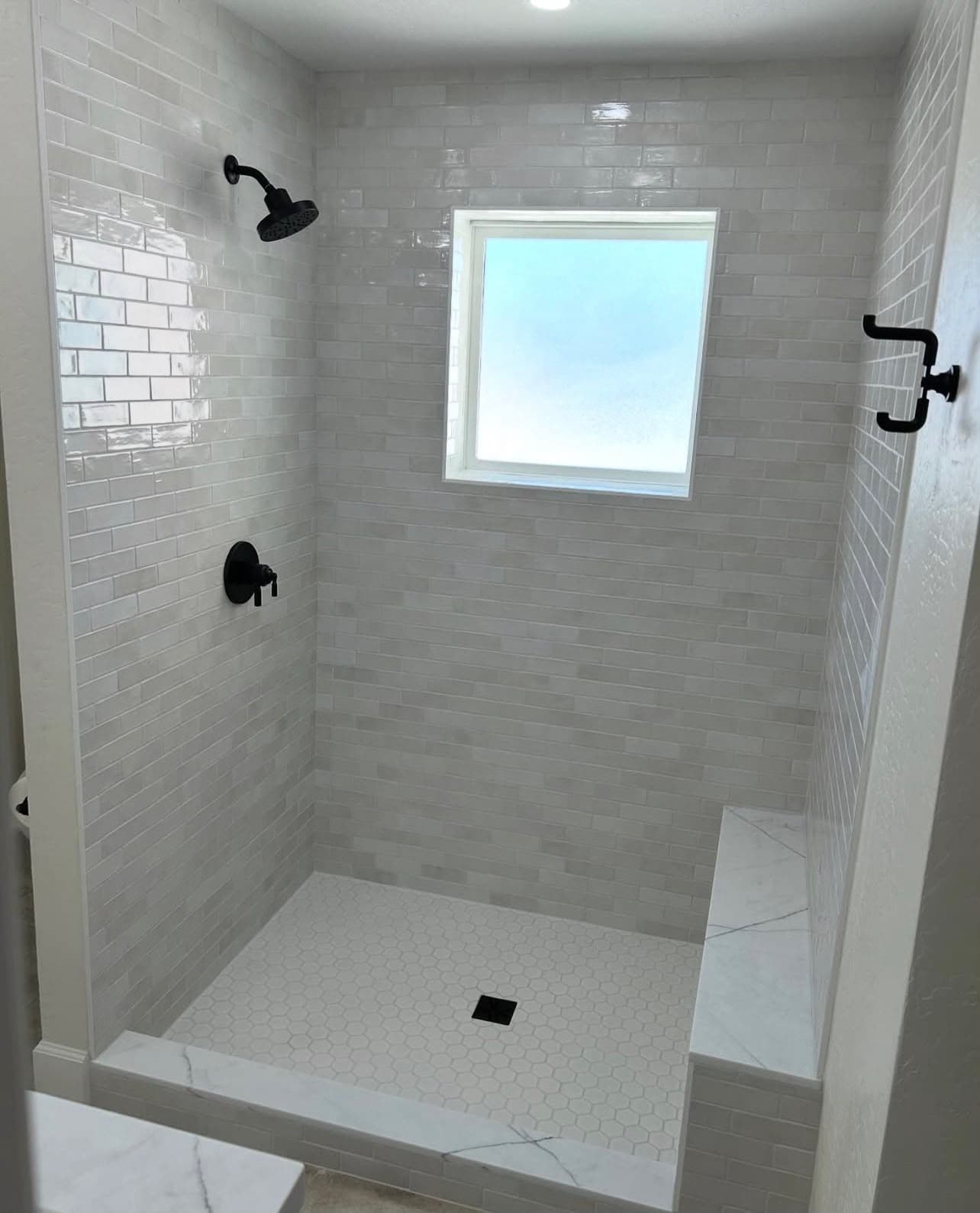 Walk-in shower with white subway tile walls, hexagon floor, and built-in bench installed by Costa Bathroom Remodel in Apollo Beach, Florida